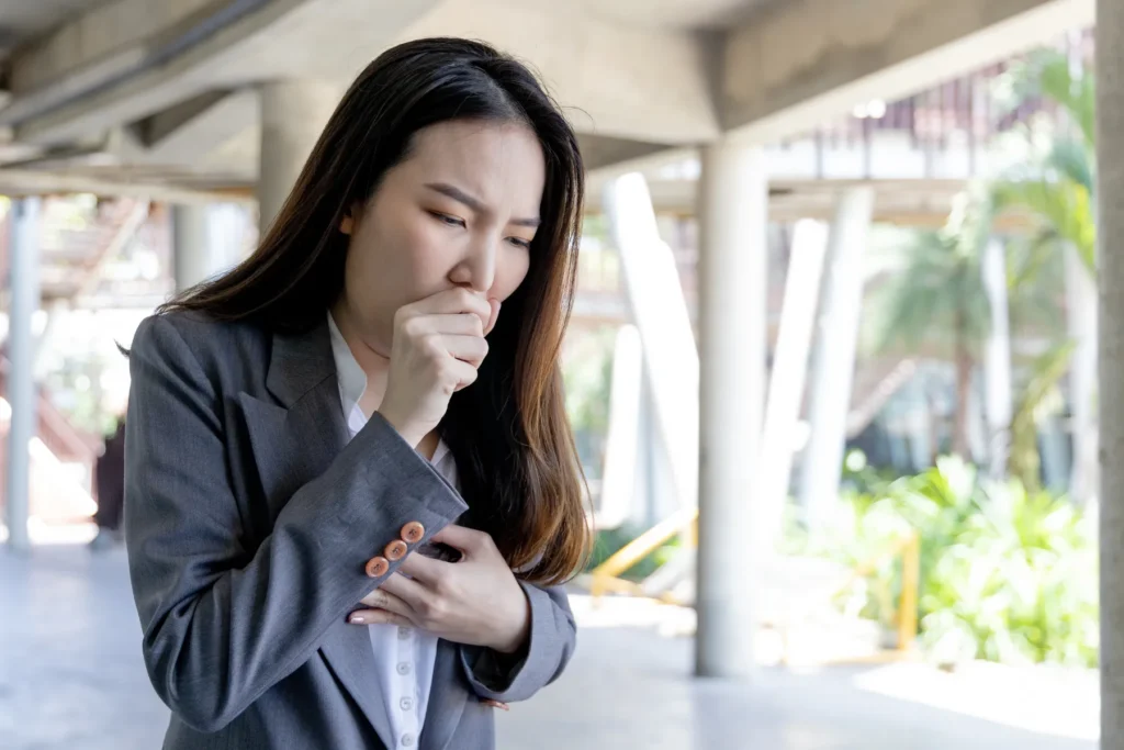 Woman outdoors who is seen coughing