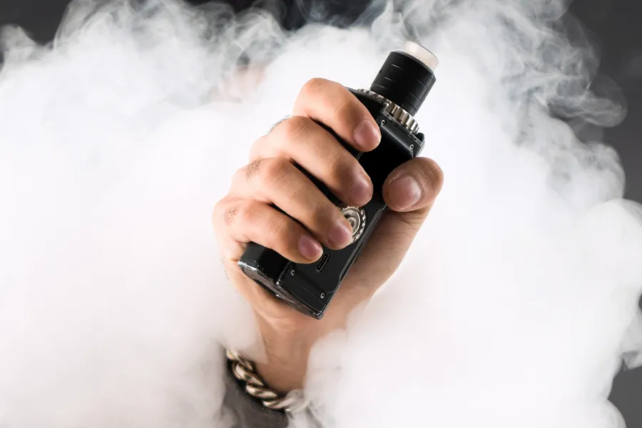 Hand holding vape coming through smoke