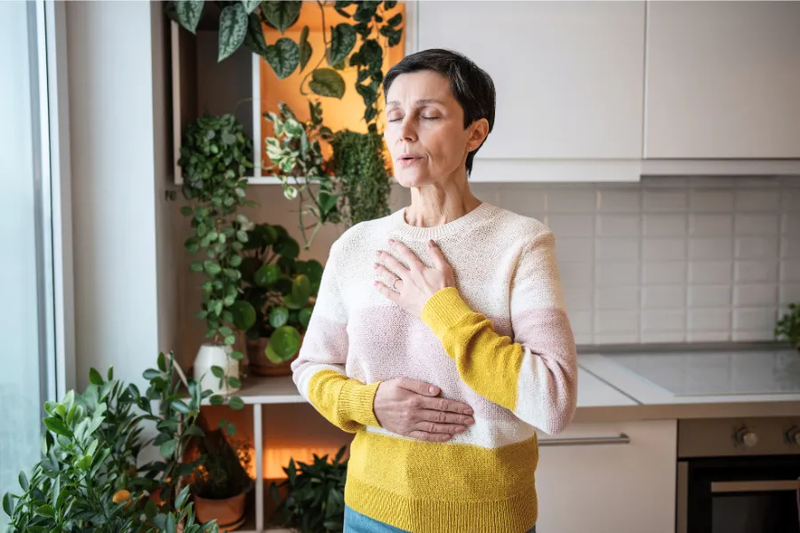 Older woman in sweater taking a deep breath in modern kitchen